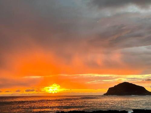 a sunset over the ocean with an island in the distance at Charming Country Cottage just a few steps from the beach! in Waianae