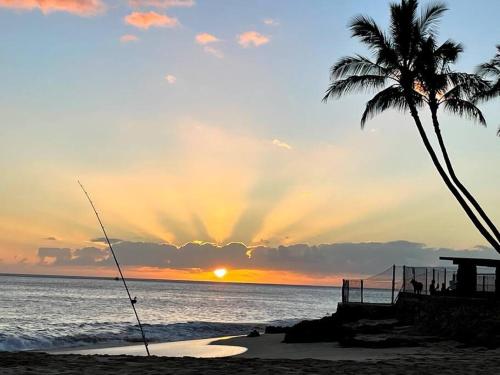a palm tree and a fishing rod on the beach at sunset at Charming Country Cottage just a few steps from the beach! in Waianae