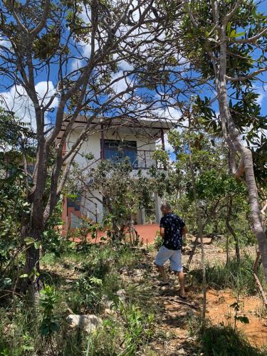 a man standing in front of a house behind trees at Chales Estrela Veadeiros in Alto Paraíso de Goiás