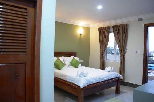 a bedroom with a bed with white sheets and green pillows at Neakru Guesthouse and Restaurant in Kampot