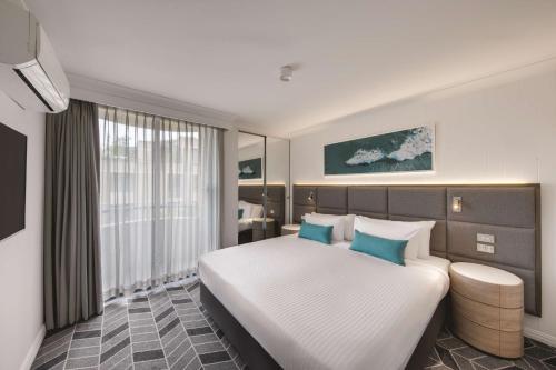 1 dormitorio con 1 cama blanca grande con almohadas azules en Adina Apartment Hotel Coogee Sydney en Sídney