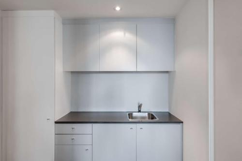 Adina Apartment Hotel Wollongong في ولونغونغ: مطبخ مع دواليب بيضاء ومغسلة