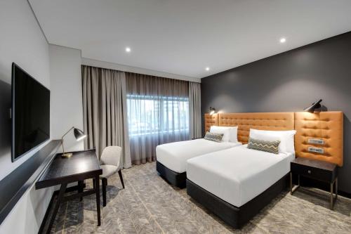 a hotel room with two beds and a desk and a television at Vibe Hotel North Sydney in Sydney