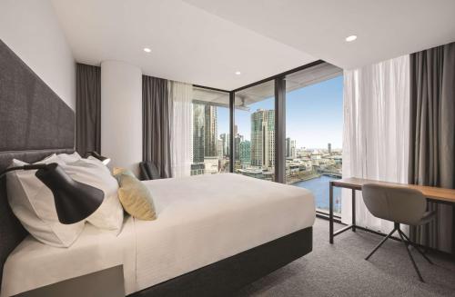 a bedroom with a bed and a desk with a large window at Vibe Hotel Melbourne in Melbourne