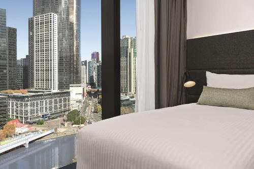 a bedroom with a bed and a view of a city at Vibe Hotel Melbourne in Melbourne