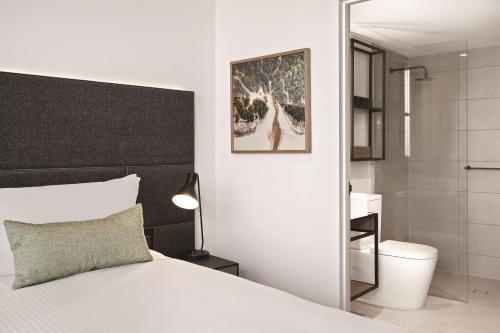 a bedroom with a white bed and a bathroom at Vibe Hotel Melbourne in Melbourne