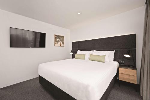 a bedroom with a large white bed and a tv at Vibe Hotel Melbourne in Melbourne