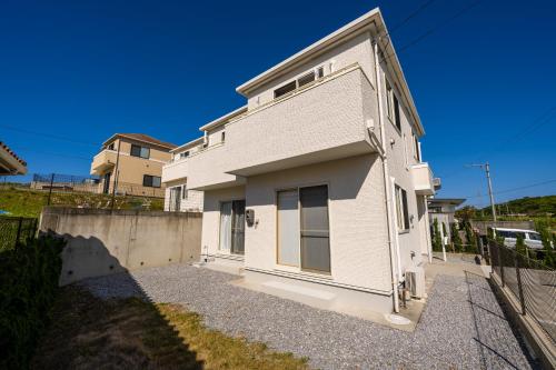 a white house on a gravel driveway at 最大12人築浅物件 南部を満喫したい方に1番のおすすめ宿 無料駐車場3台 サウスウィンドハウス in Inamine