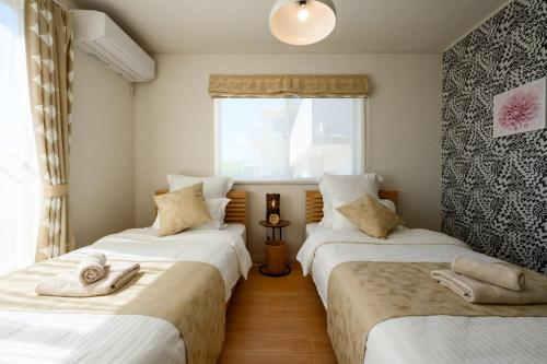 two twin beds in a room with a window at 最大12人築浅物件 南部を満喫したい方に1番のおすすめ宿 無料駐車場3台 サウスウィンドハウス in Inamine