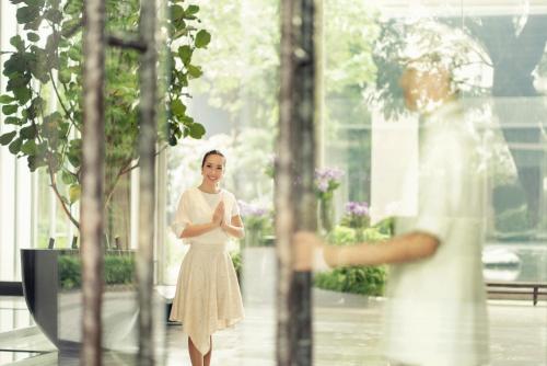 a woman in a white dress standing in front of a window at Four Seasons Hotel Bangkok at Chao Phraya River in Bangkok