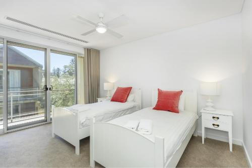 a white bedroom with two beds and a window at Cottesloe Beach Haven in Perth