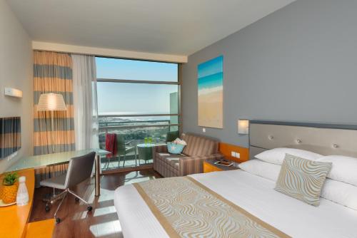 a hotel room with a bed and a desk and a window at Leonardo Plaza Ashdod in Ashdod