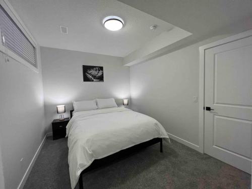 a white bedroom with a bed and two lamps at Cozy New Suite in NW Calgary in Calgary