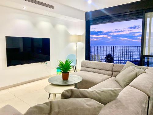 a living room with a couch and a large window at Beach Place Apartments in Haifa