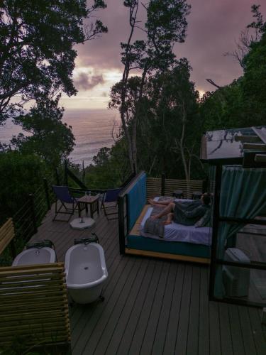 eine Person, die auf einem Bett auf einer Terrasse mit einer Badewanne liegt in der Unterkunft The Stargazing Cube - Misty Mountain Reserve in Stormsrivier