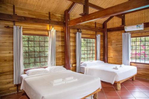 two beds in a room with wooden walls and windows at Phu Quoc Valley Sen Bungalow in Phu Quoc