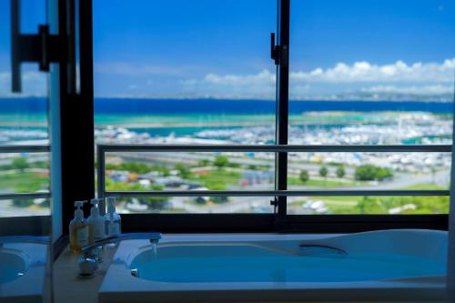 La salle de bains est pourvue d'une baignoire et d'une fenêtre avec vue. dans l'établissement Moon Ocean Ginowan Hotel & Residence, à Ginowan