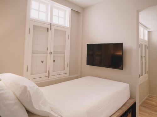 a white bedroom with a bed and a flat screen tv at Hotel 1900 Chinatown in Singapore