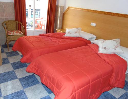 two beds in a hotel room with red sheets at Hotel Libertador in Cullera