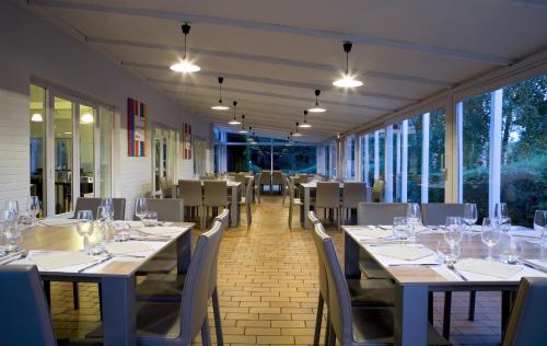 a dining room with tables and chairs and windows at Kyriad Lille Est - Villeneuve d'Ascq in Villeneuve d'Ascq