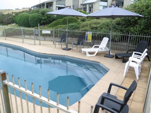 a swimming pool with chairs and umbrellas next to a fence at 15 Whitecrest Great Ocean Road Resort - Ocean View in Apollo Bay