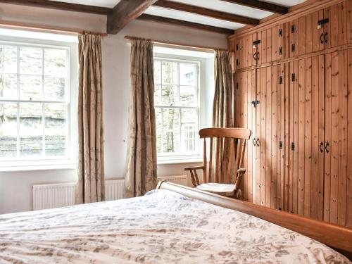 a bedroom with a bed and a chair and windows at Stable Cottage in Askrigg