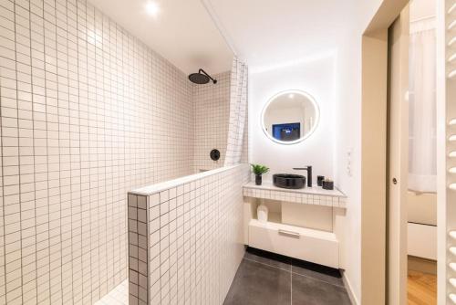a white tiled bathroom with a sink and a mirror at La suite du Graou in Metz