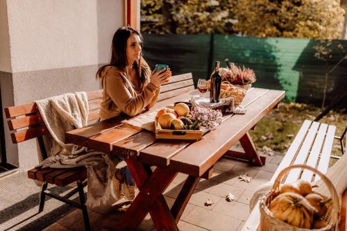 a woman sitting at a picnic table with a cell phone at Domki RADAWA na Kliszówce in Radawa