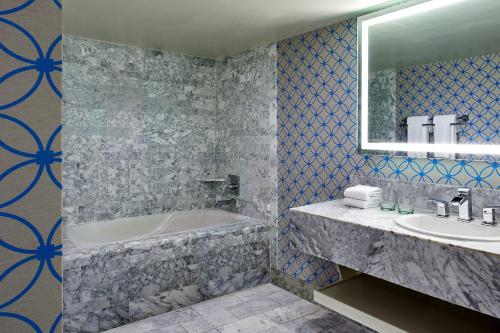 a bathroom with a tub and a sink and a mirror at Le Meridien Delfina Santa Monica in Los Angeles