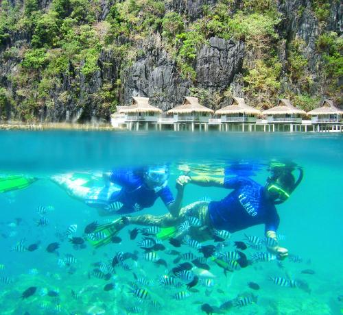 two people swimming in the water in front of a resort at El Nido Resorts Miniloc Island in El Nido