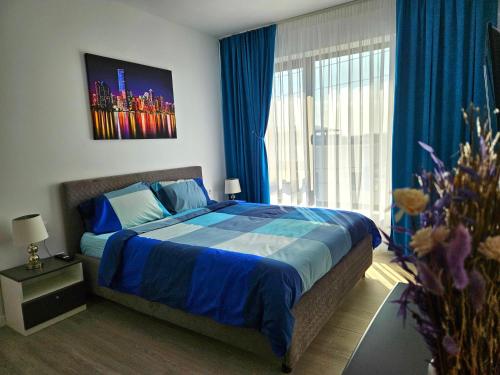sypialnia z łóżkiem z niebieską pościelą i oknem w obiekcie Apartament Ștrand w mieście Râmnicu Vâlcea