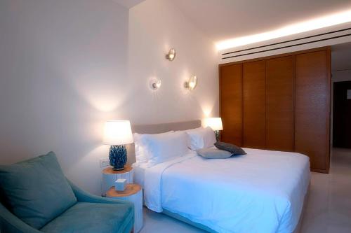 a bedroom with a bed and a blue chair at Domes Miramare, a Luxury Collection Resort, Corfu - Adults Only in Moraitika