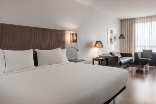 a bedroom with a large white bed and a living room at AC Hotel Coslada Aeropuerto by Marriott in Coslada