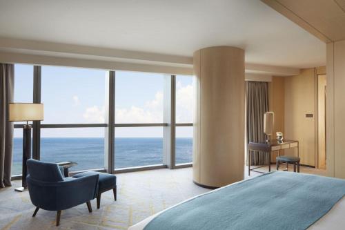 um quarto com uma cama, uma cadeira e janelas em The St. Regis Qingdao em Qingdao