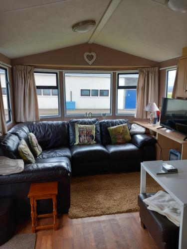 a living room with a black leather couch and a table at Melody Brooks Caravan Park in Portknockie