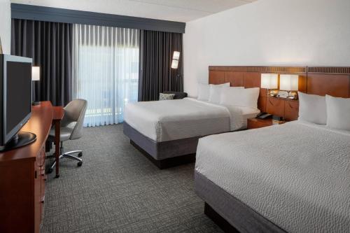 a hotel room with two beds and a desk and a television at Courtyard by Marriott Memphis East/Park Avenue in Memphis
