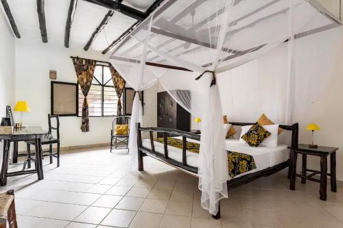a bedroom with a canopy bed and a desk at Zarafa House in Diani Beach