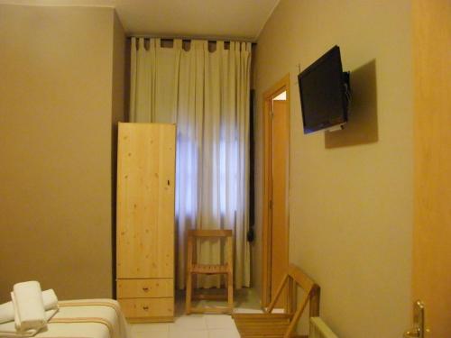 Habitación con cama, TV y silla. en Pensión Corona, en Zaragoza