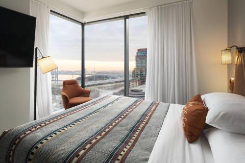 ルイスビルにあるMoxy Louisville Downtownのベッドと大きな窓が備わるホテルルームです。
