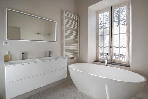 La salle de bains blanche est pourvue d'une grande baignoire et d'une fenêtre. dans l'établissement Domaine Mont-Riant à Jurançon, à Jurançon