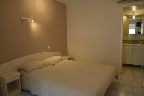 a bedroom with a white bed and a kitchen at Hôtel Des Arceaux in Saint-Sever