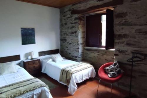 a bedroom with two beds and a red chair at Casa de Campo - Casa da Ribeira in Serapicos