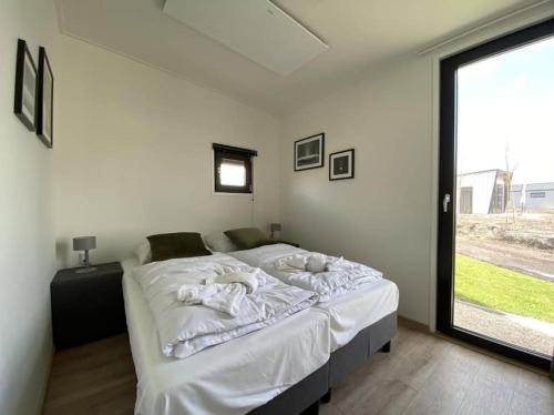1 dormitorio con 1 cama blanca grande y ventana en Tiny vakantiehuis aan het water met eigen steiger en airco, en Kampen
