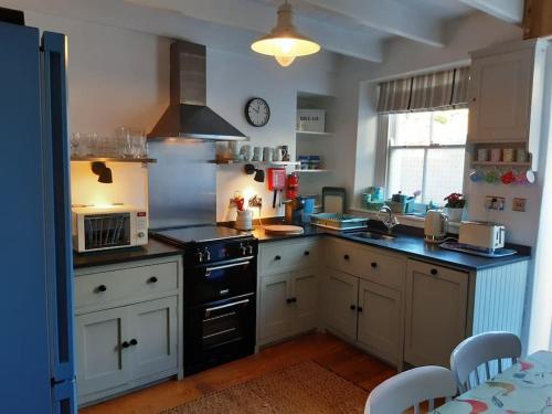 eine Küche mit weißen Schränken und einem schwarzen Herd mit Backofen in der Unterkunft Corvus - Beautiful cottage half a mile from Mousehole in Penzance