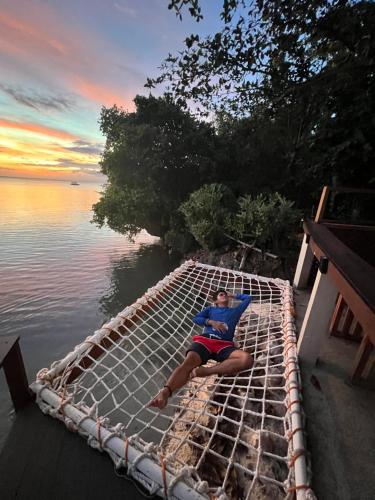 a man laying on a hammock on a boat in the water at White Bada Guesthouse in Siquijor