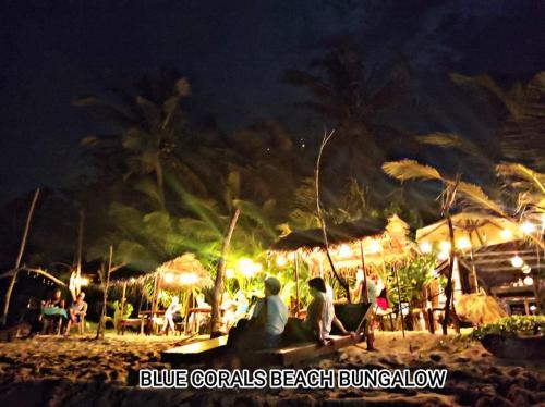 a group of people sitting on the beach at night at Blue Corals Beach Bungalow in Madihe East