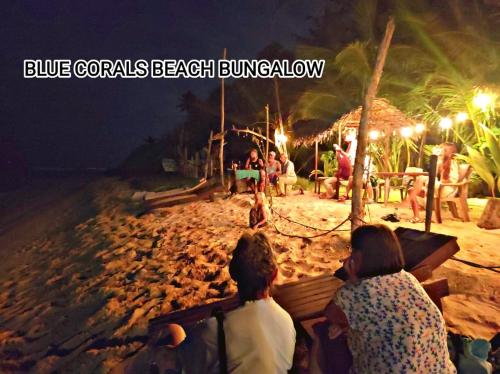 a group of people sitting on a beach at night at Blue Corals Beach Bungalow in Madihe East