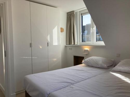 een witte slaapkamer met een bed en een raam bij Vakantiewoning 1 aan zee, 400 meter van het strand in Zoutelande