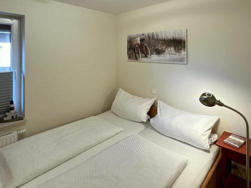 a bedroom with a bed with white sheets and a lamp at Ferienwohnung *Haus Ose* in Wittdün