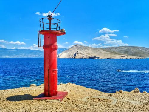 a red pole in the sand next to the water at Ferienhaus mit Meerblick & Pool in Baška - Villa-Planina in Baška